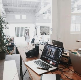 A bright, modern workspace featuring laptops, a camera, and a drawing tablet in an indoor office.